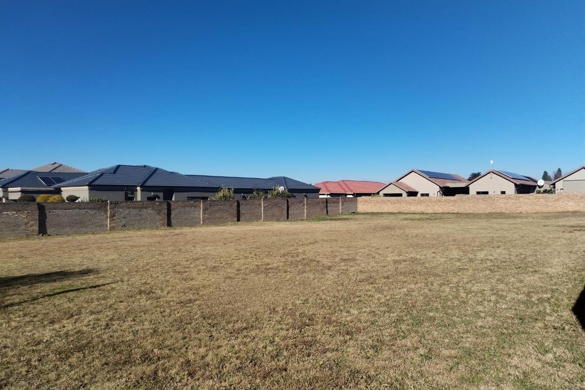A vacant residential plot featuring level grass terrain and perimeter brick boundary walls, situated within an established suburban neighborhood.