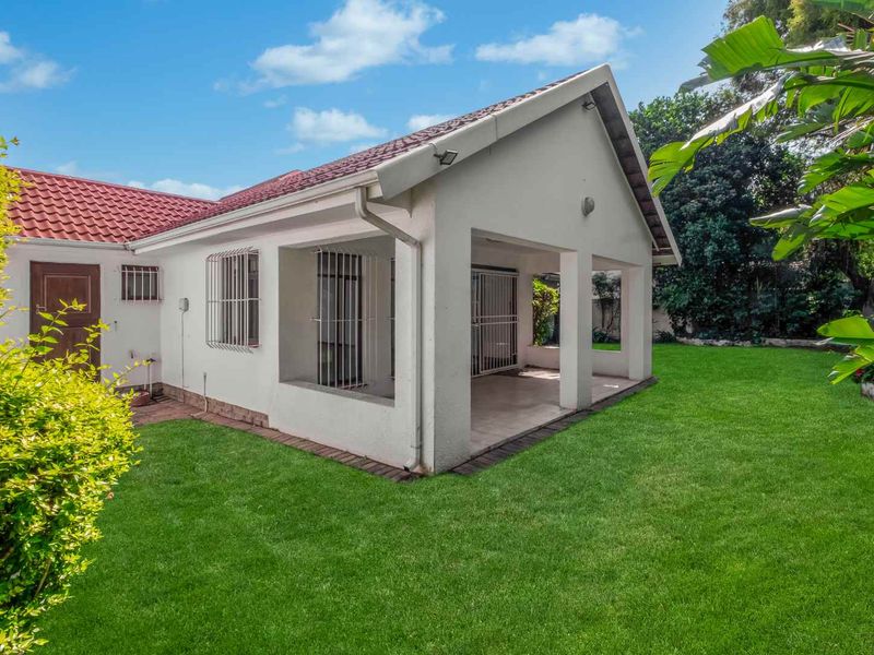 Rear view of the property featuring a covered patio, tiled roof, and a well-maintained garden lawn.