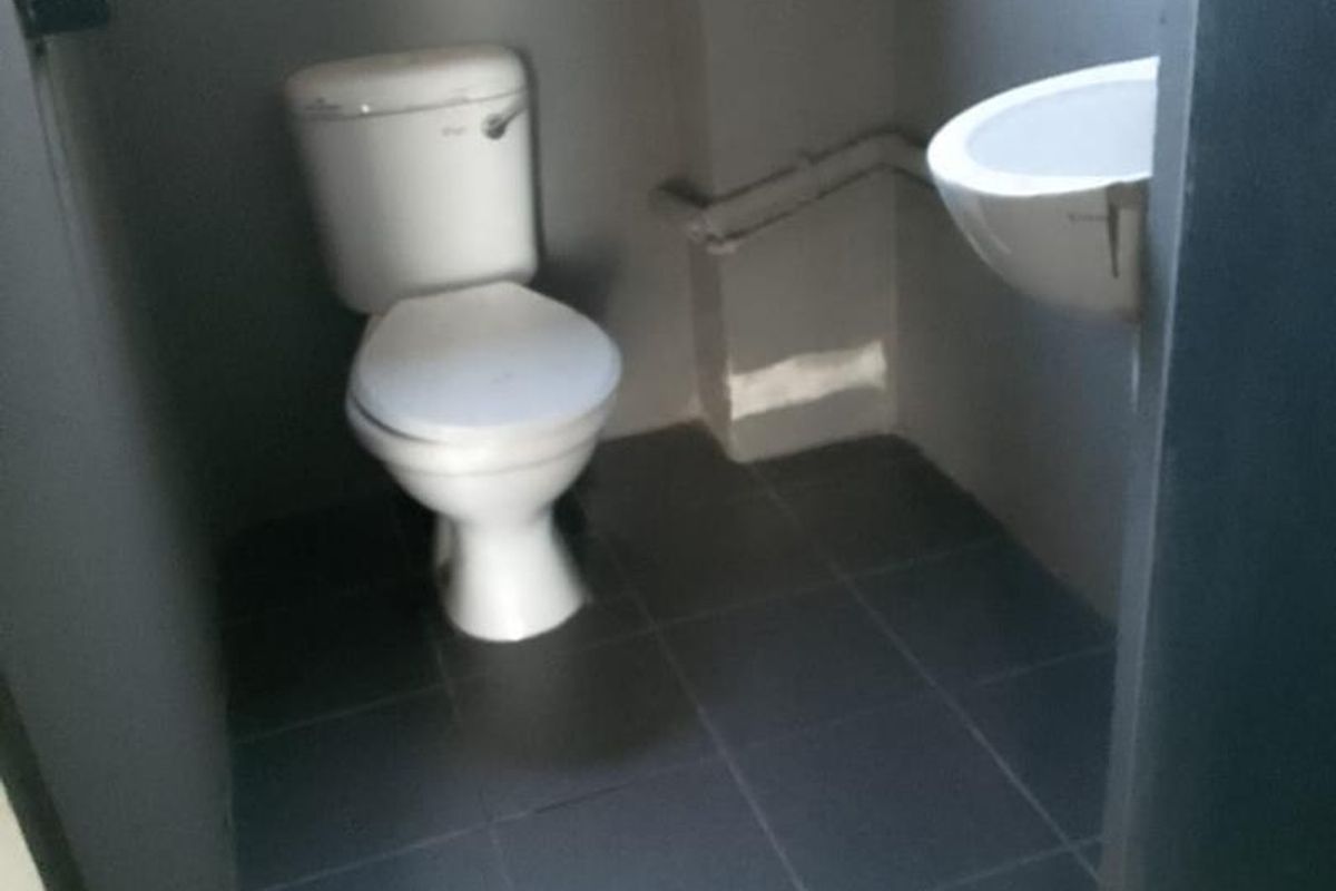 A compact functional restroom featuring a standard toilet and wall-mounted basin with dark floor tiling.