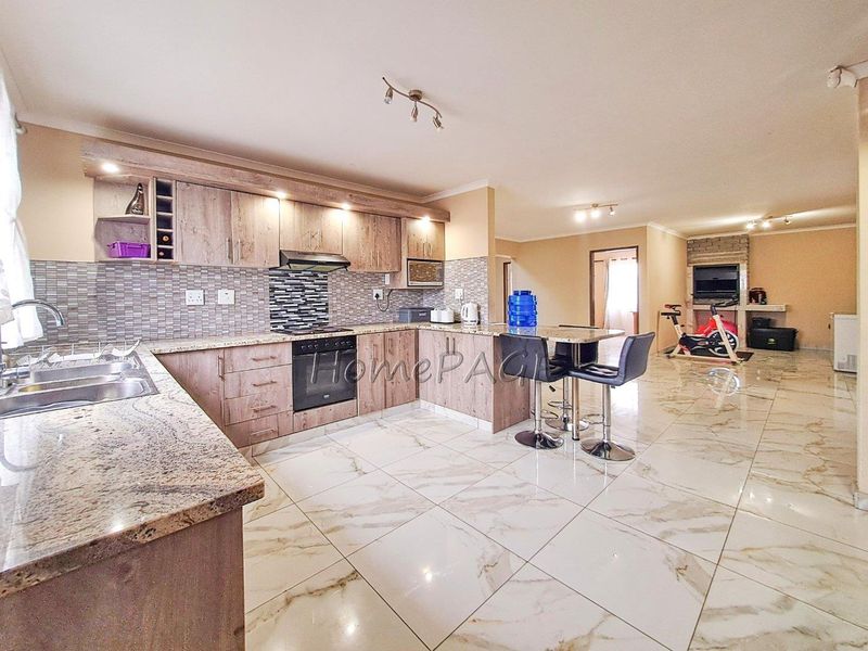 Spacious open-plan kitchen and living area featuring modern cabinetry, granite countertops, tiled flooring, and a built-in fireplace.