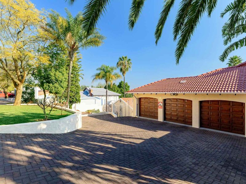Front view of the property featuring a triple garage with wooden doors, a paved driveway, and a well-maintained garden area.