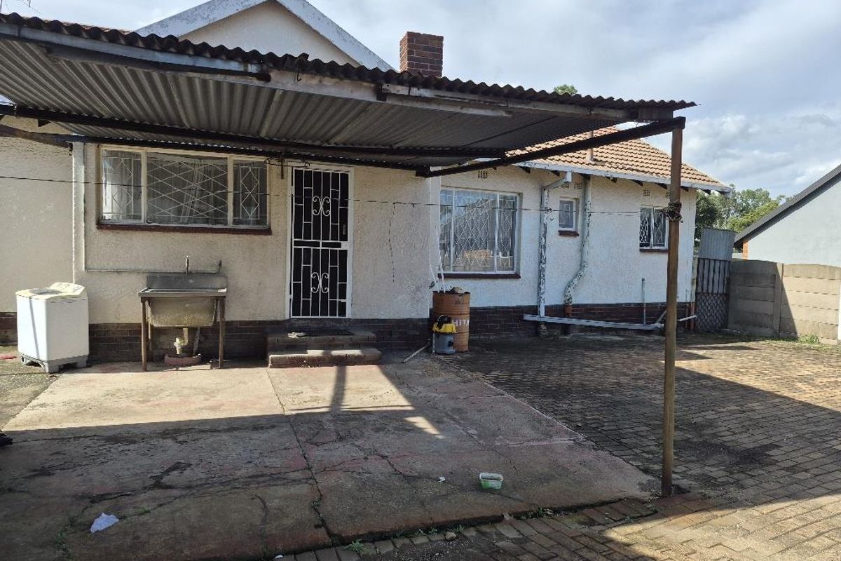 Rear exterior view of the house featuring a covered patio area, paved courtyard, and external utility sink.