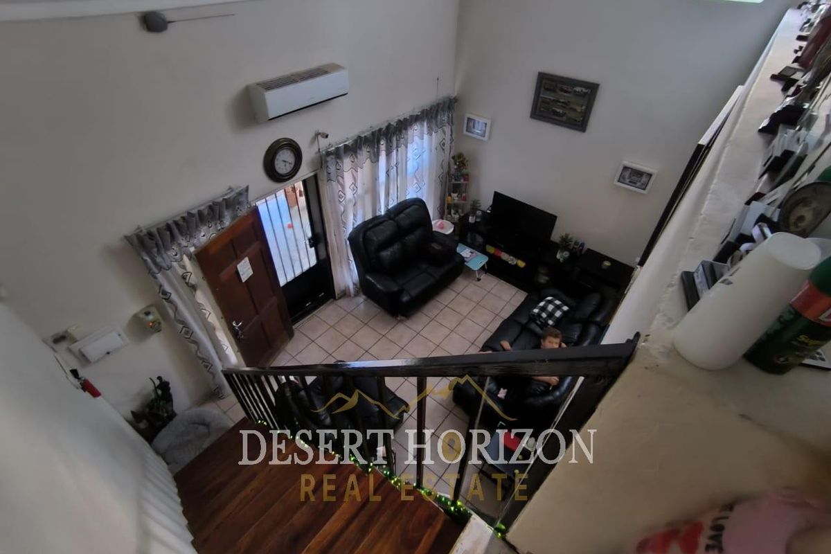 High-angle view of a living room featuring tiled flooring, a split-system air conditioner, and a staircase with a dark wood handrail.