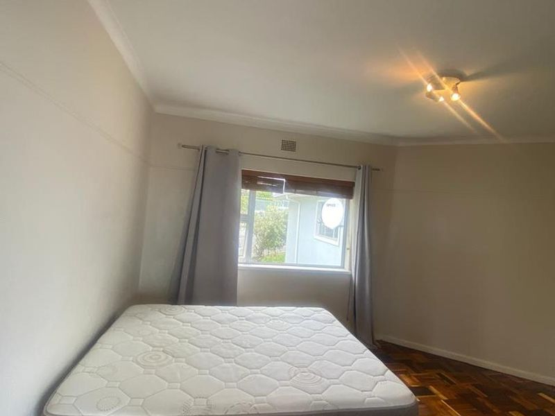A bedroom featuring classic parquet flooring, neutral walls, and a ceiling-mounted light fixture, offering a clean and functional space.