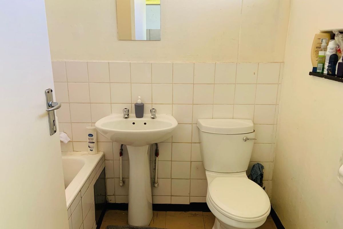A functional bathroom featuring a pedestal washbasin, toilet, and bathtub with tiled splashbacks, currently requiring cosmetic updates and maintenance.