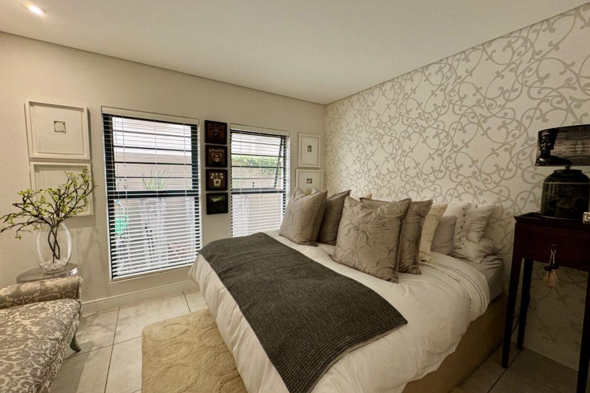 A well-maintained bedroom featuring tiled flooring, large windows with fitted blinds, and a decorative feature wall with patterned wallpaper.