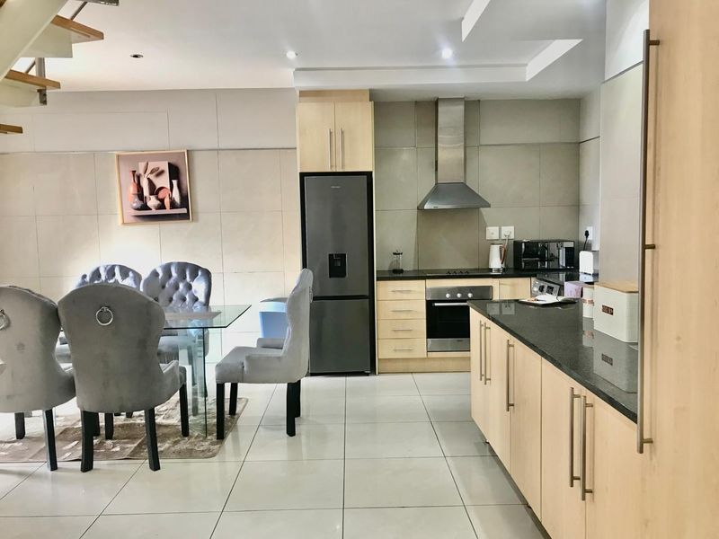 Modern open-plan kitchen and dining area featuring light wood cabinetry, granite countertops, stainless steel appliances, and sleek tiled flooring.