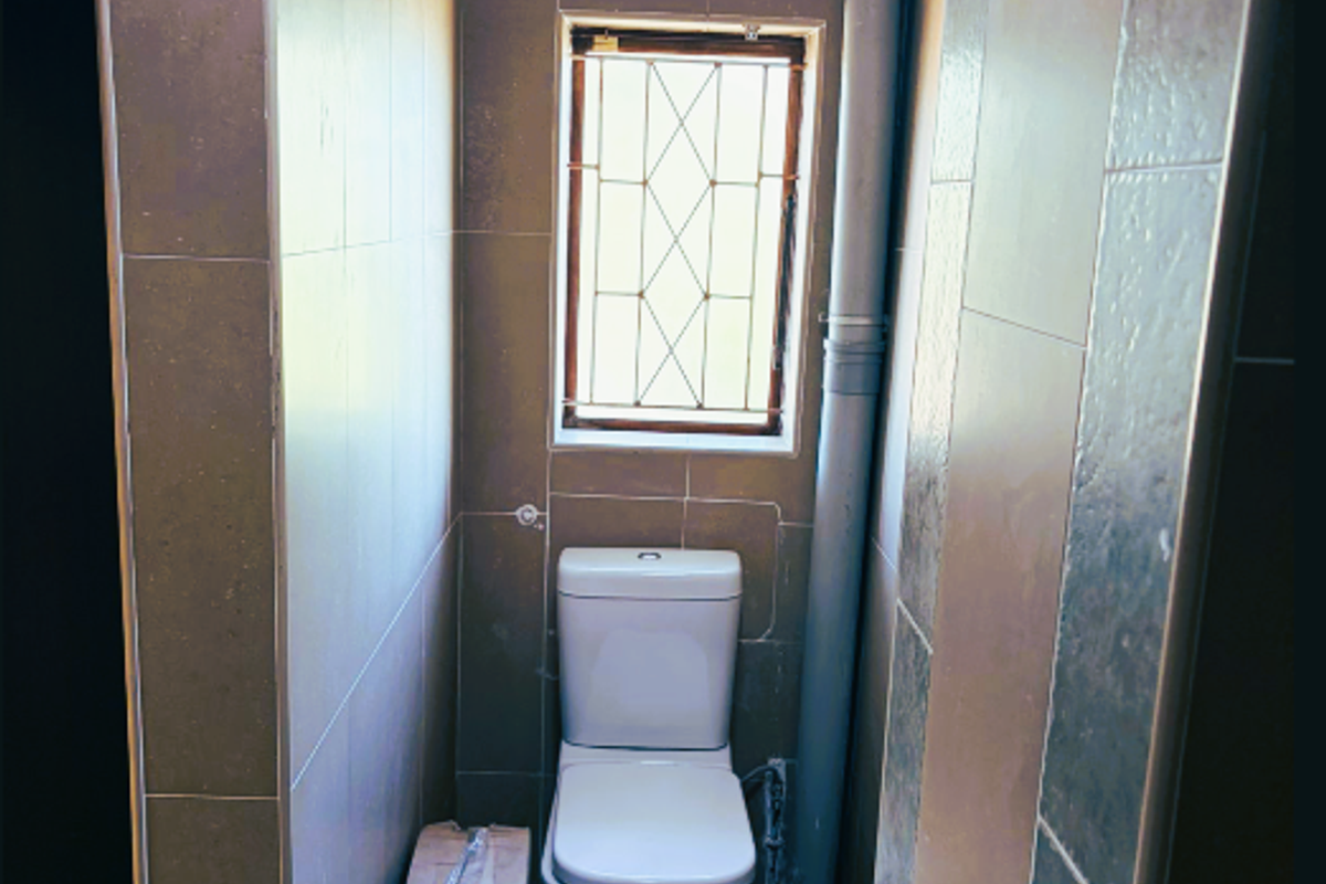 A compact office restroom featuring a wall-mounted basin, a standard toilet, and full-height wall tiling with an exposed vertical plumbing pipe.