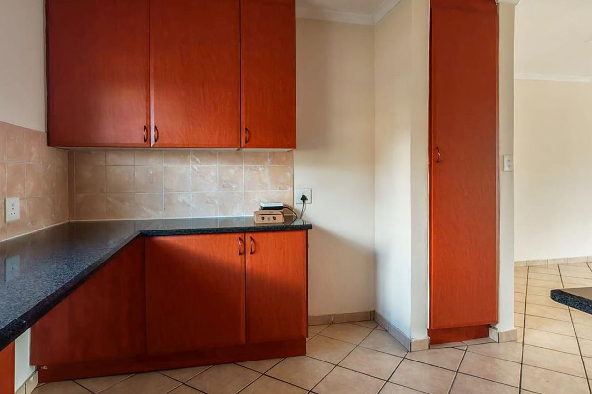 A functional kitchen area featuring wood-finish cabinetry, granite countertops, and neutral ceramic floor tiles, offering a clean and practical layout.