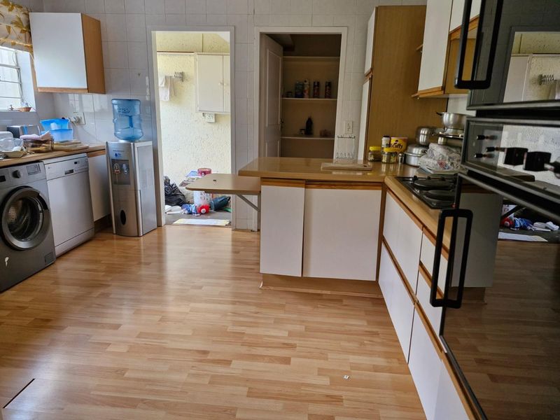 A functional kitchen featuring laminate flooring, built-in cabinetry, a gas hob, and a built-in oven, with an adjacent pantry and utility area.