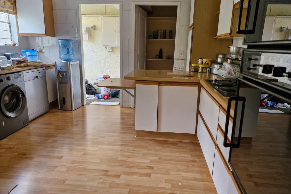 A functional kitchen featuring laminate flooring, built-in cabinetry, a gas hob, and a built-in oven, with an adjacent pantry and utility area.