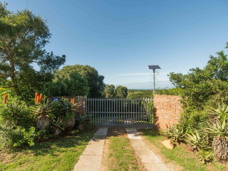 A secure gated entrance featuring brick pillars, a metal security gate, and solar-powered lighting, set within a landscaped garden environment.