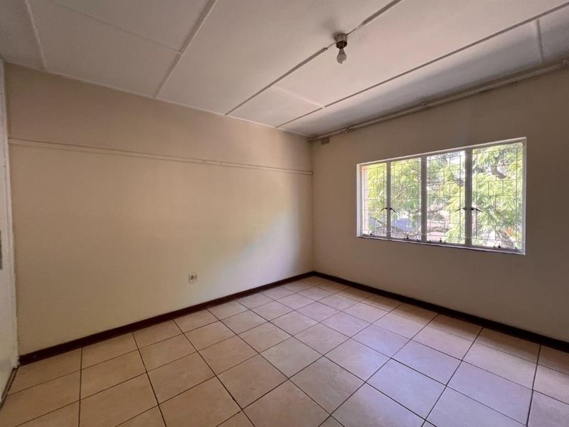 An empty bedroom featuring tiled flooring, a built-in cupboard, and a window fitted with security bars.