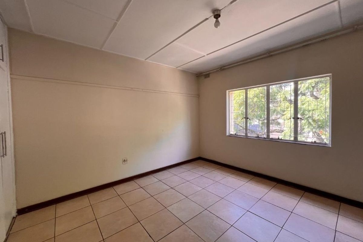 An empty bedroom featuring tiled flooring, a built-in cupboard, and a window fitted with security bars.