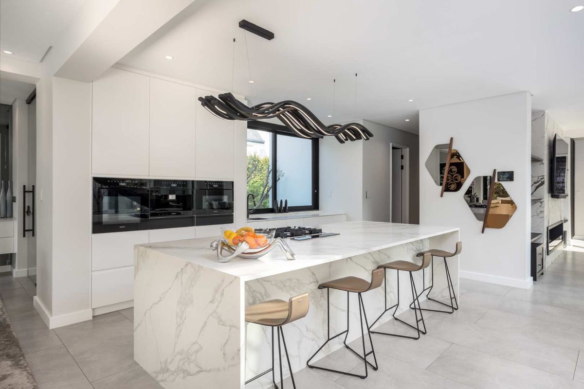 Modern luxury kitchen featuring a large marble island, high-end built-in appliances, handleless cabinetry, and sophisticated designer lighting.