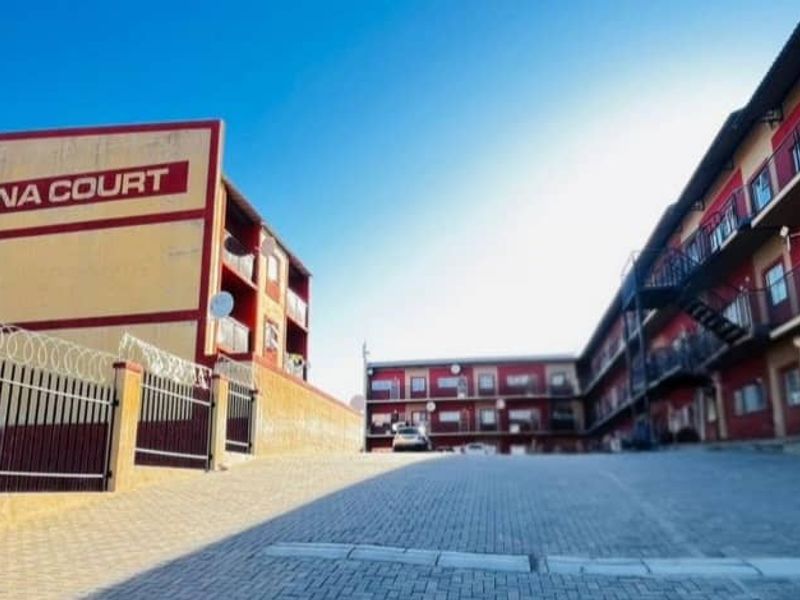 Exterior view of Havana Court apartment complex featuring a paved driveway, security fencing, and multi-level residential units with balconies.