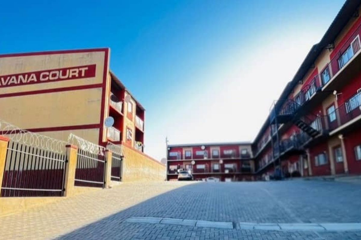Exterior view of Havana Court apartment complex featuring a paved driveway, security fencing, and multi-level residential units with balconies.