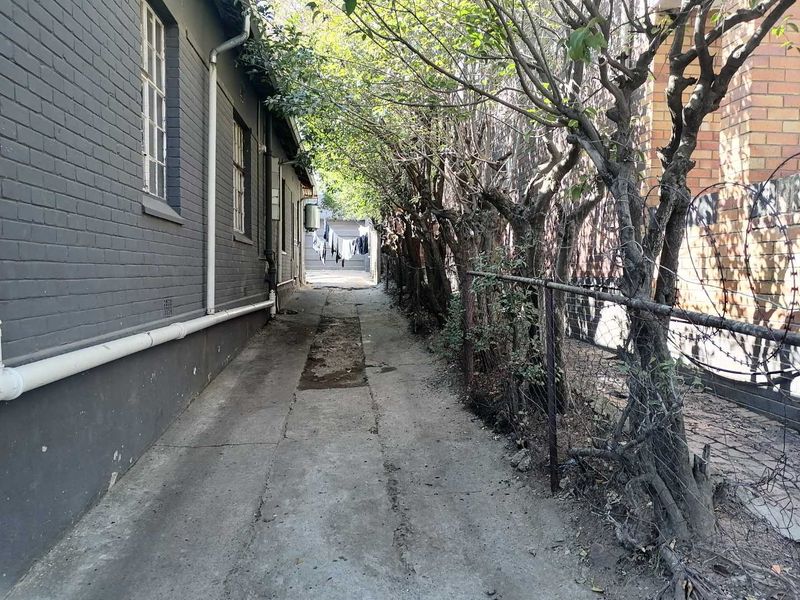 A narrow exterior side passage featuring a concrete walkway, brick wall, and perimeter fencing with barbed wire.