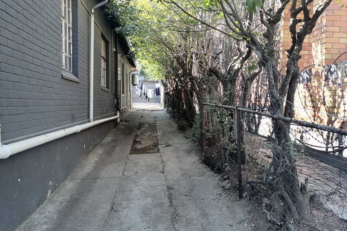 A narrow exterior side passage featuring a concrete walkway, brick wall, and perimeter fencing with barbed wire.