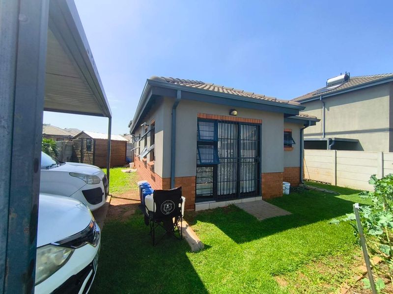 Rear view of the property featuring a tiled roof, brick and plaster facade, security gates, and a covered carport area with a small garden.