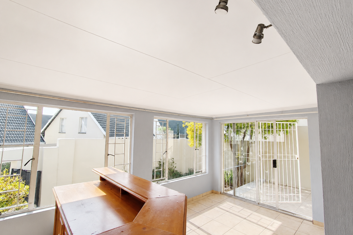 Bright living area featuring tiled floors, track lighting, and large windows with direct access to an outdoor patio space.