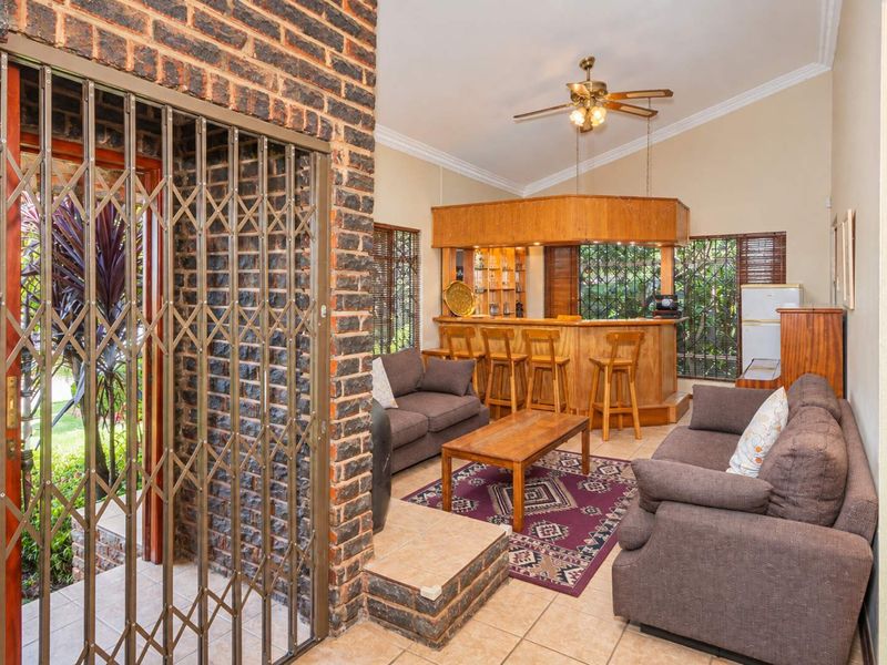 A spacious living area featuring a built-in wooden bar, vaulted ceilings, brick feature wall, and tiled flooring with direct access to the exterior.