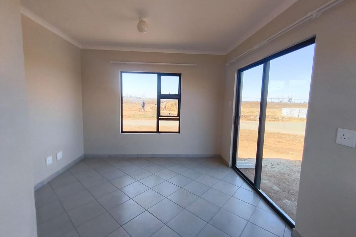 A bright, empty living area featuring neutral tiled flooring, large aluminium-framed windows, and a sliding glass door providing access to the exterior.