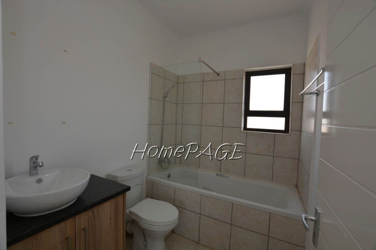 A functional bathroom featuring a built-in bathtub with a glass shower screen, a vanity cabinet with a basin, and a toilet.