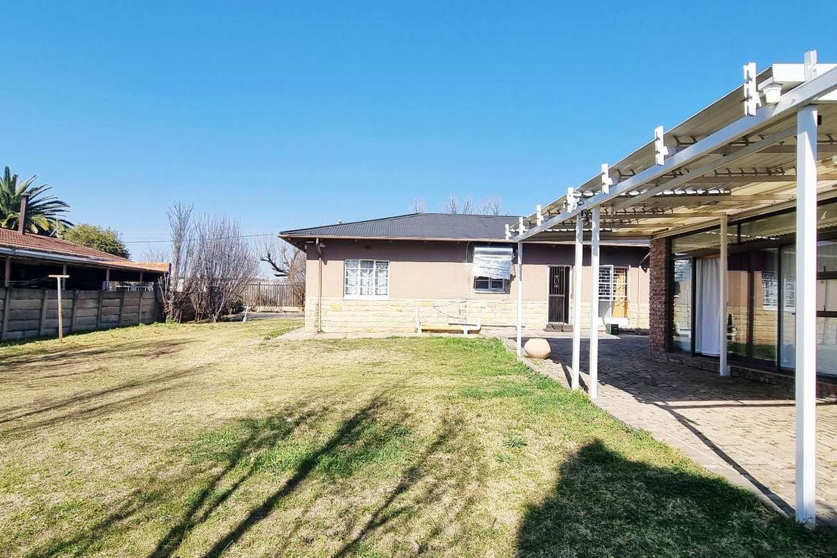 Spacious rear garden featuring a paved covered patio area, brick boundary walls, and established lawn, offering potential for outdoor living and landscaping.