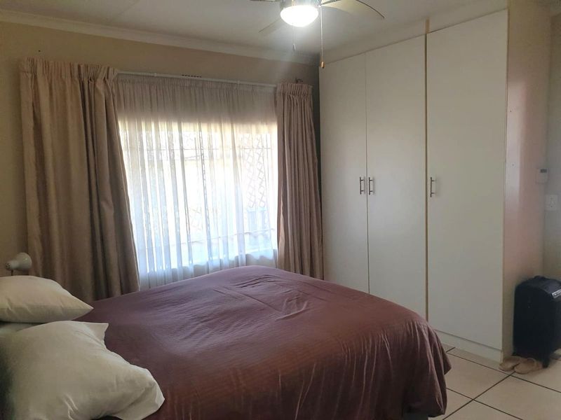 A functional bedroom featuring built-in cupboards, tiled flooring, and a ceiling fan, offering a comfortable and practical living space.