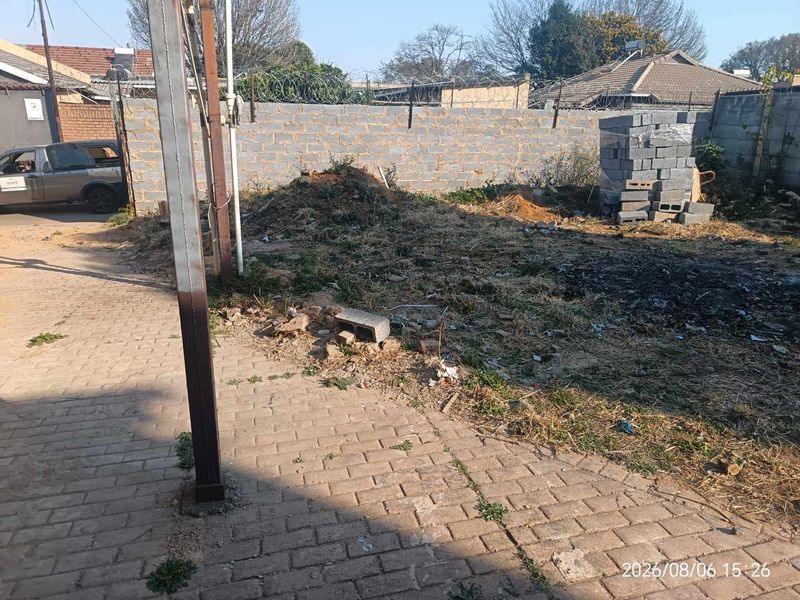 A view of the rear yard area featuring a perimeter wall with security fencing, paved section, and unimproved ground requiring landscaping.