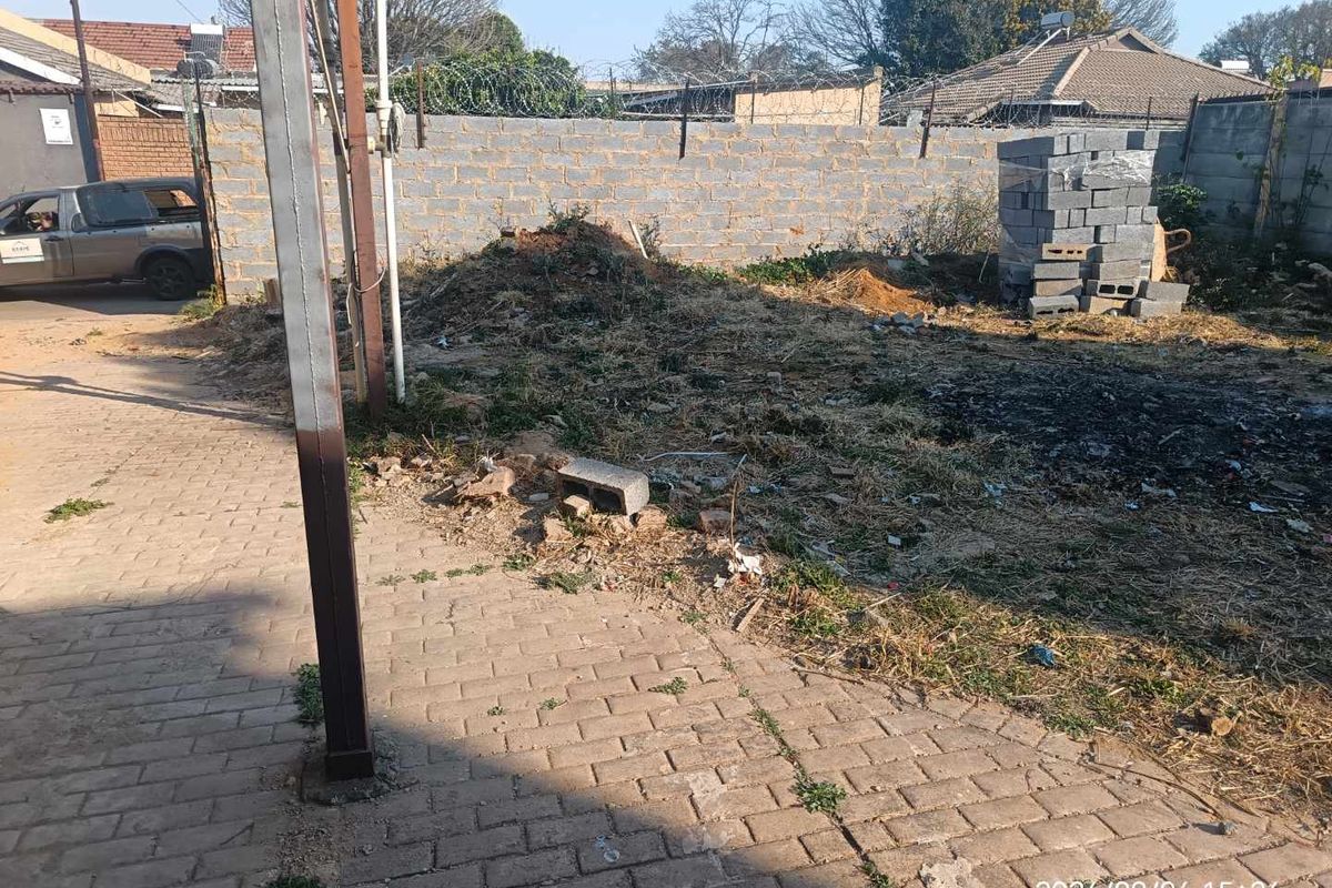 A view of the rear yard area featuring a perimeter wall with security fencing, paved section, and unimproved ground requiring landscaping.
