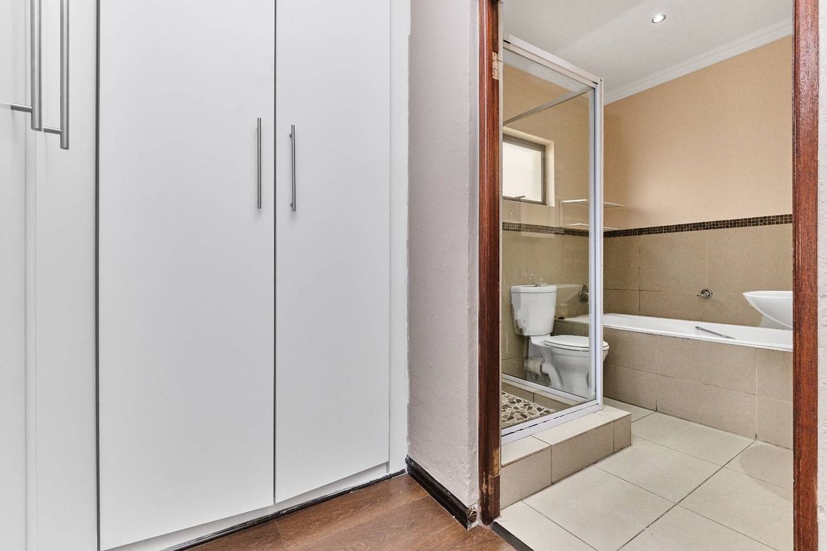 A bathroom featuring a built-in bathtub, glass-enclosed shower, and toilet, adjacent to a hallway with built-in cabinetry.