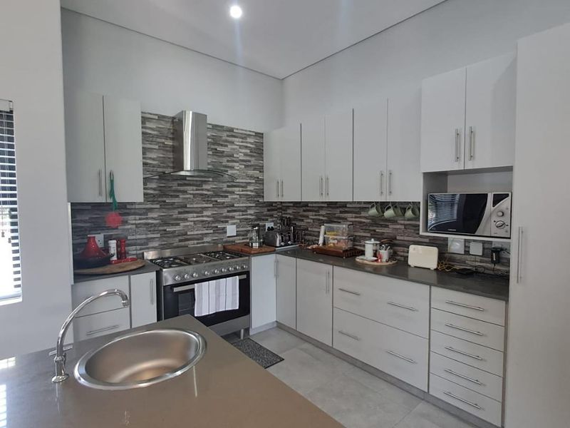Modern kitchen featuring white cabinetry, stone countertops, a stainless steel gas stove with extractor fan, and a convenient island with an undermount sink.