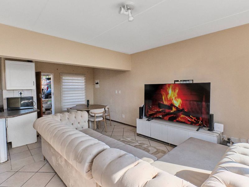 Open-plan living area featuring tiled flooring, a compact kitchen with built-in cabinetry, and direct access to the exterior.