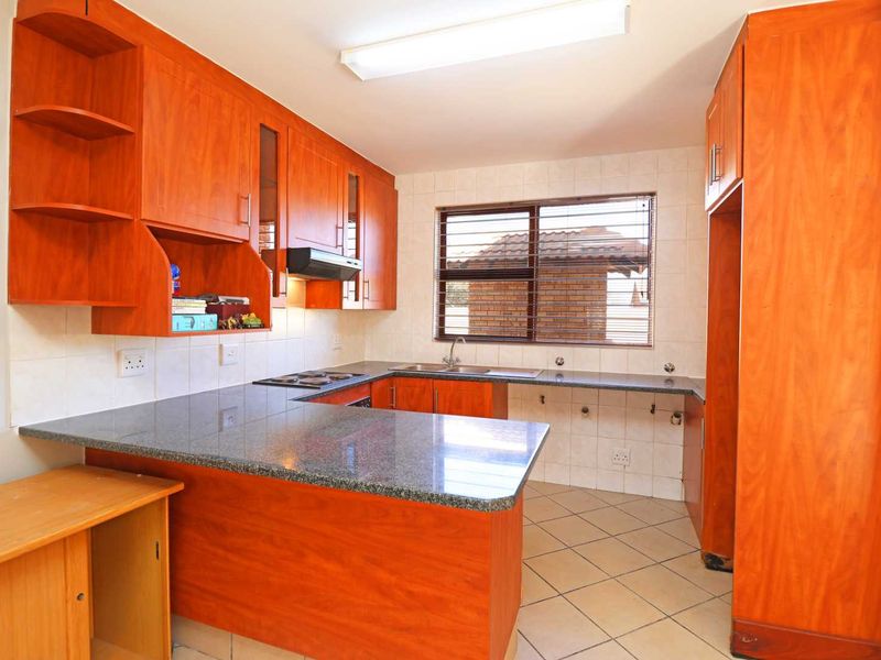 A functional kitchen featuring granite countertops, wooden cabinetry, an electric hob, and an integrated extractor fan with tiled flooring and backsplash.