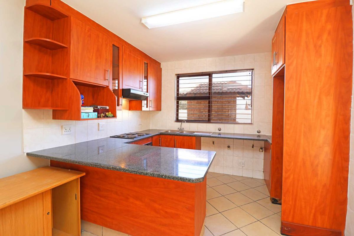 A functional kitchen featuring granite countertops, wooden cabinetry, an electric hob, and an integrated extractor fan with tiled flooring and backsplash.