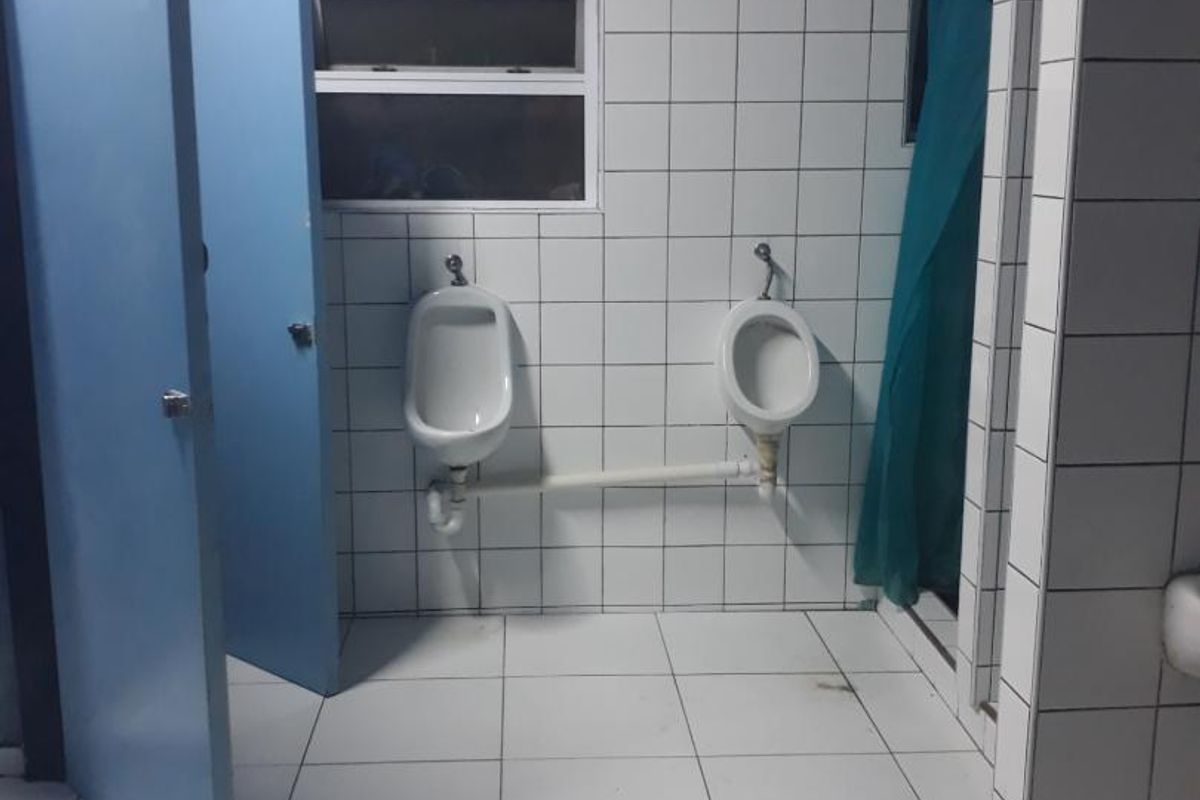 A functional commercial restroom facility featuring tiled walls and floors, equipped with two wall-mounted urinals and a partitioned shower area.