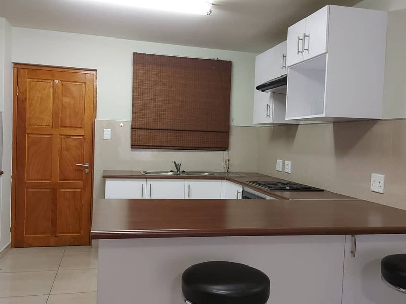 A functional kitchen featuring white cabinetry, dark laminate countertops, a built-in hob with extractor fan, and tiled flooring.