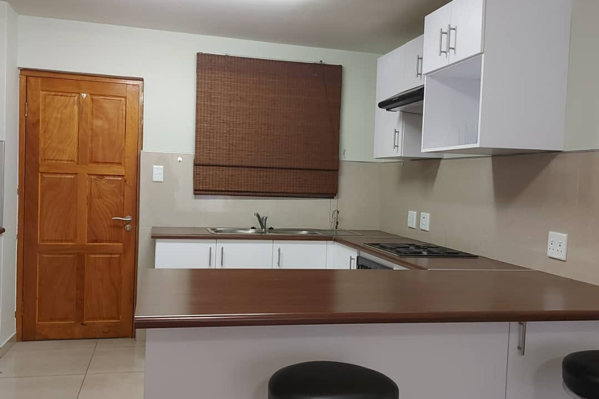 A functional kitchen featuring white cabinetry, dark laminate countertops, a built-in hob with extractor fan, and tiled flooring.
