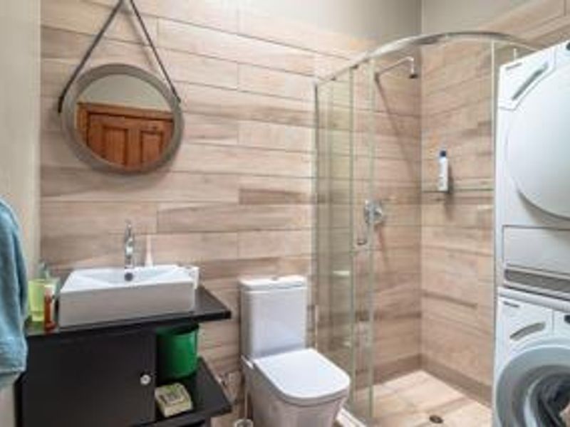Modern bathroom featuring wood-look wall tiles, a vessel sink vanity, a glass-enclosed shower, and a stacked laundry unit.