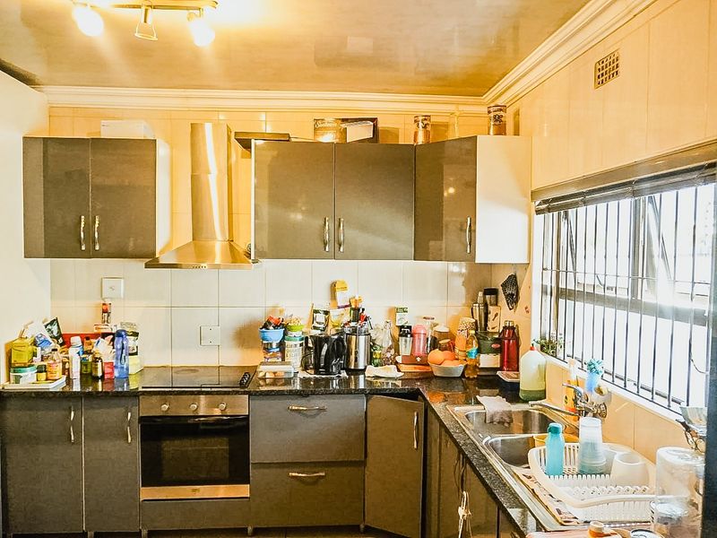 A functional kitchen featuring dark grey cabinetry, granite countertops, a built-in oven with hob, and a double basin sink with security bars on the window.