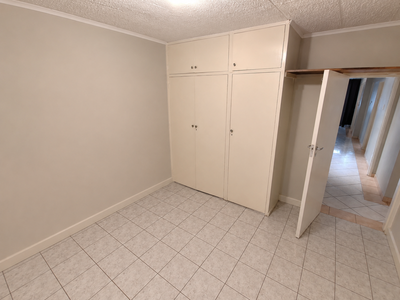 An empty bedroom featuring tiled flooring, built-in cupboards with overhead storage, and a textured ceiling, offering a clean canvas for personalization.