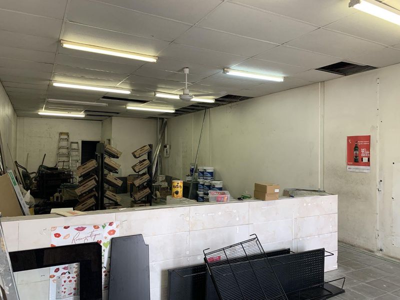 An open-plan retail space featuring a tiled service counter, suspended ceiling with integrated lighting, and significant areas requiring maintenance and finishing.
