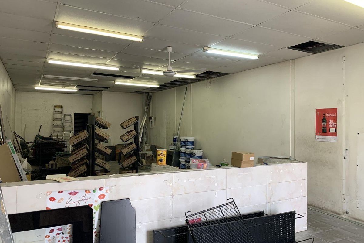 An open-plan retail space featuring a tiled service counter, suspended ceiling with integrated lighting, and significant areas requiring maintenance and finishing.