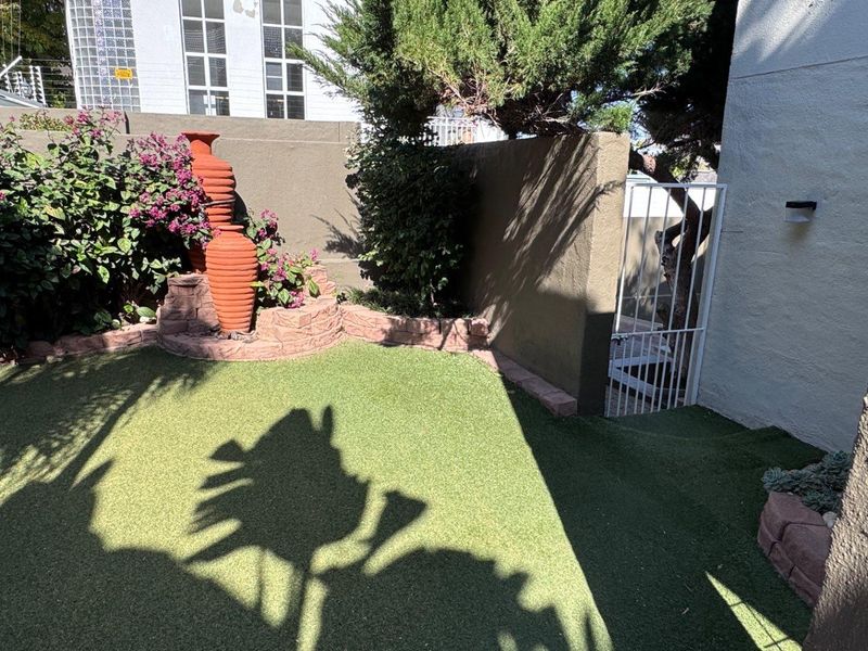 A private rear garden area featuring artificial turf, a raised stone planter bed, and a secure metal gate access point.
