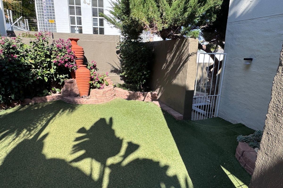 A private rear garden area featuring artificial turf, a raised stone planter bed, and a secure metal gate access point.