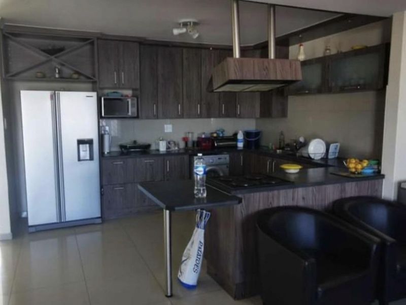 A functional kitchen featuring dark wood-look cabinetry, a breakfast bar, integrated hob, and extractor fan, with tiled flooring throughout.