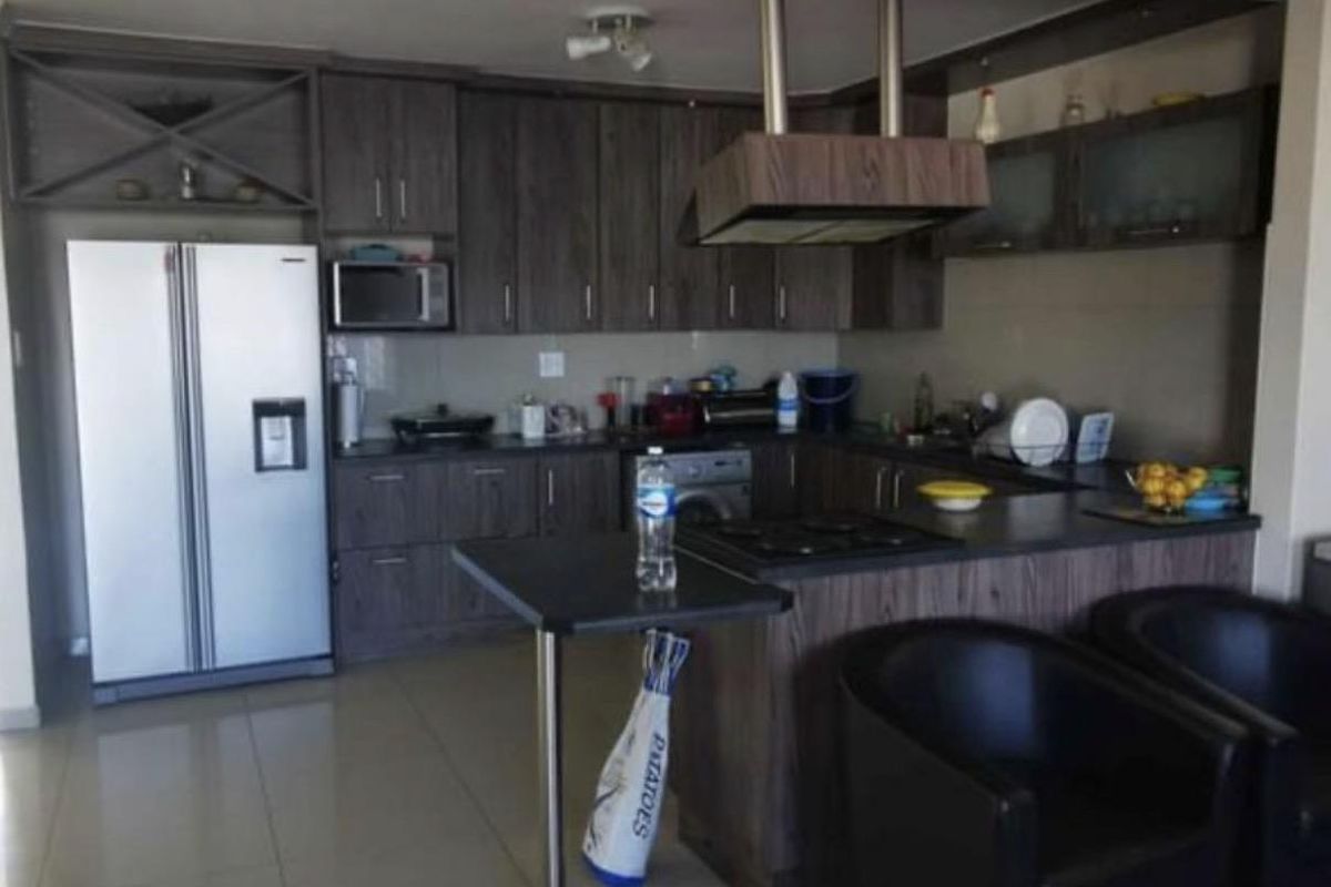 A functional kitchen featuring dark wood-look cabinetry, a breakfast bar, integrated hob, and extractor fan, with tiled flooring throughout.