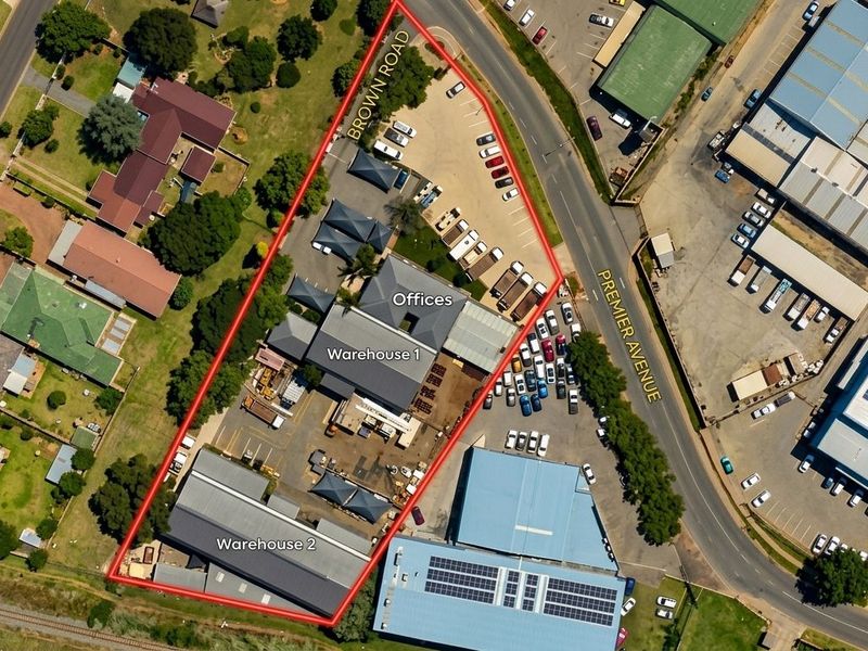 Aerial view of a commercial property featuring two warehouse buildings, an office block, and extensive paved parking facilities with dual street access.